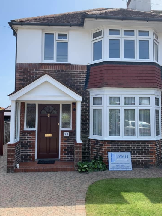 Two new white bay windows and porch on a Worthing semi with a DWD board outside